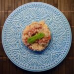 Risotto cremoso in una ciotola, guarnito con prezzemolo fresco e burro freddo da freezer accanto.